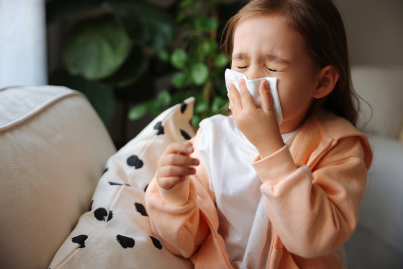 A little girl using a tissue to blow her nose.